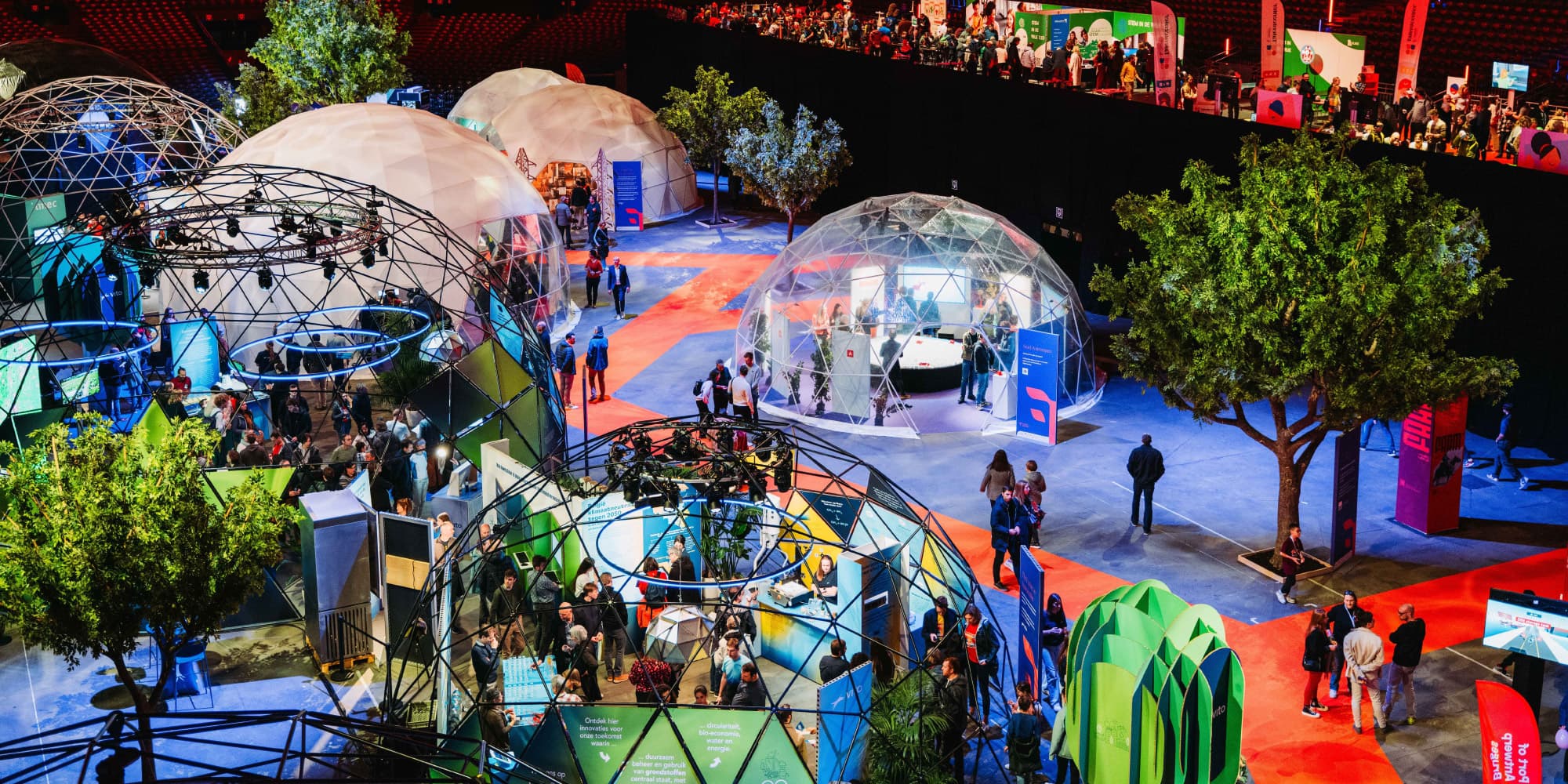 FTI-2026 Druk innovatiefestival met geodetische koepels, stands en bezoekers die exposities verkennen onder kleurrijke verlichting.