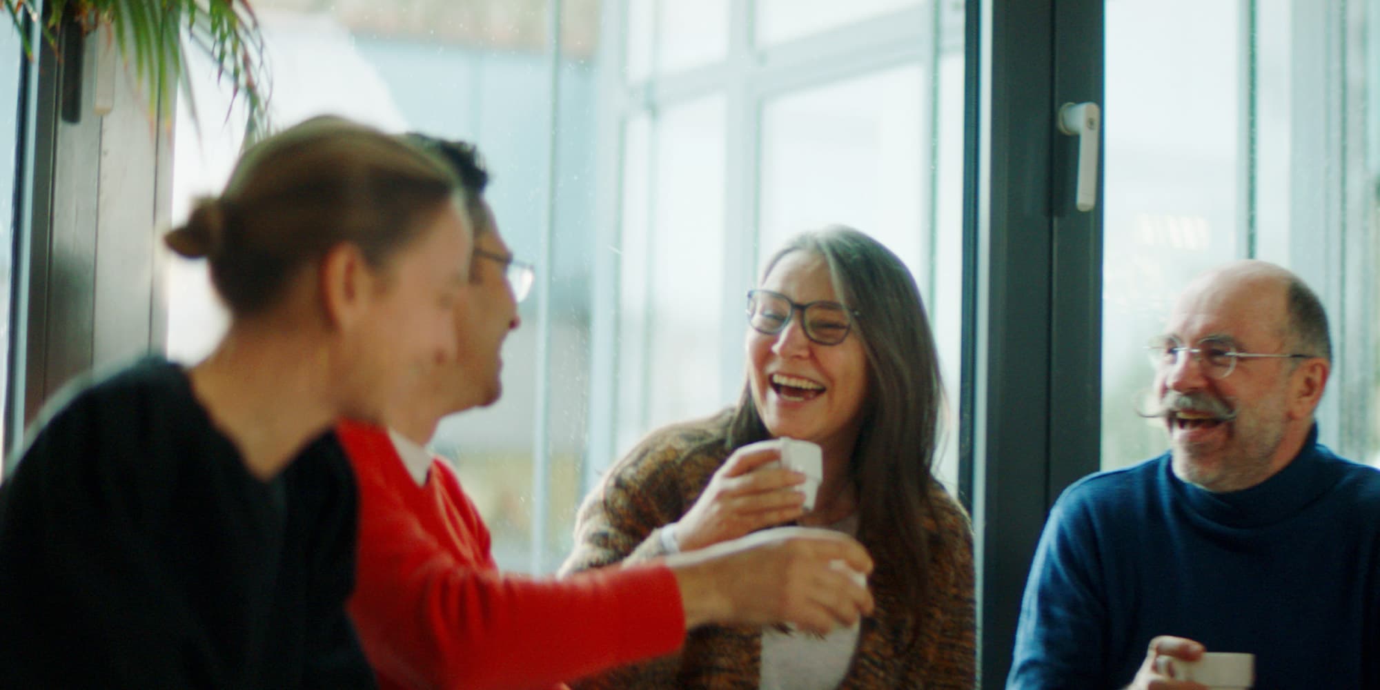 job-page Collega’s lachen samen onder het genot van koffie in een helder kantoor