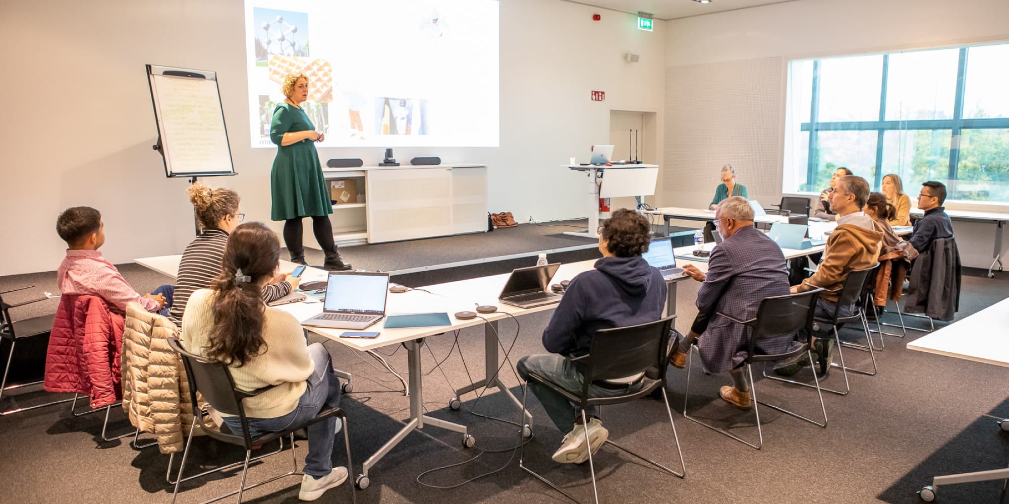 teaching Trainer die een fysieke klassikale sessie leidt met zittende deelnemers en presentatiescherm