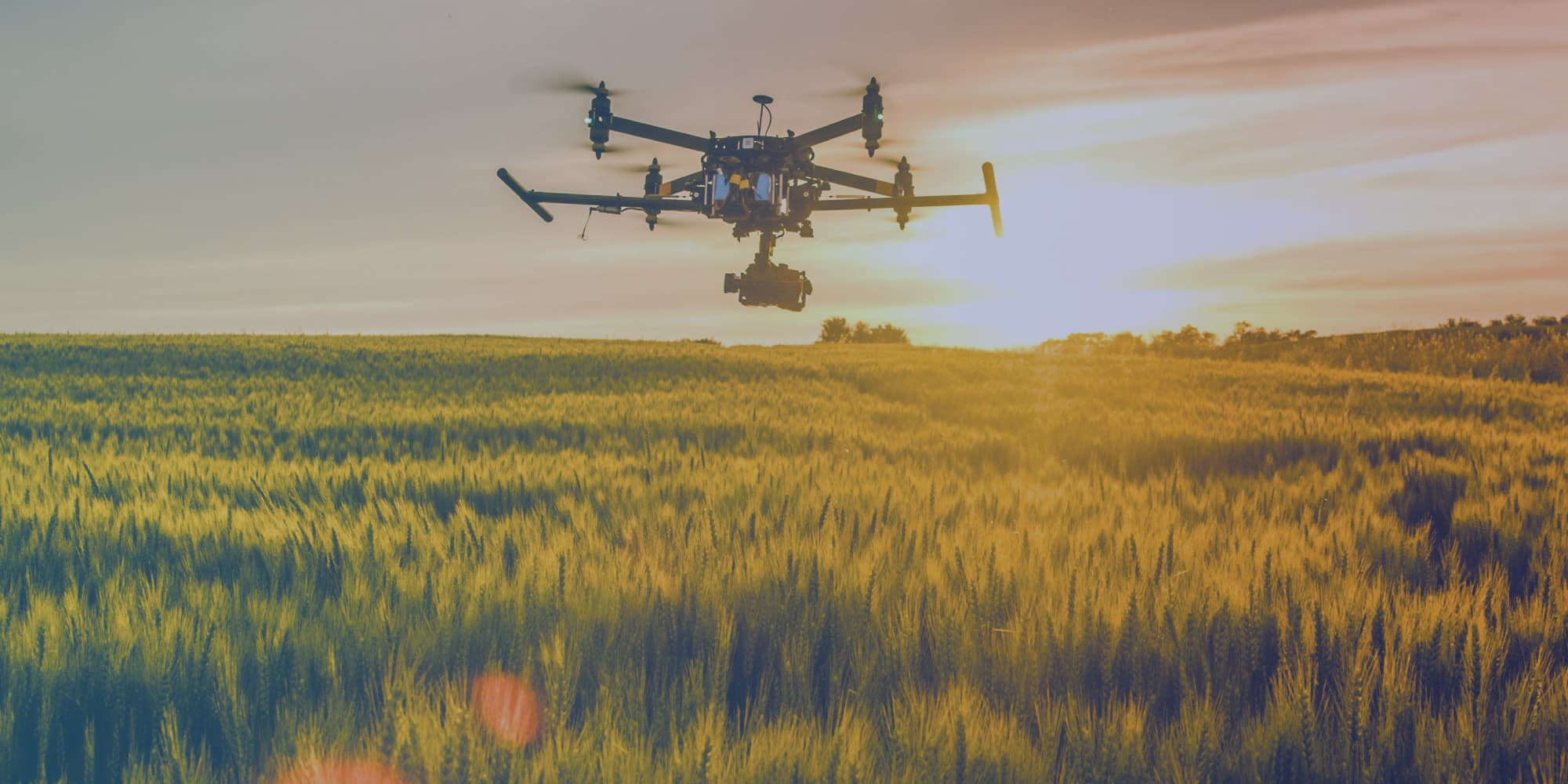 agriculture Drone flying over a crop field at sunset, with a camera suspended underneath