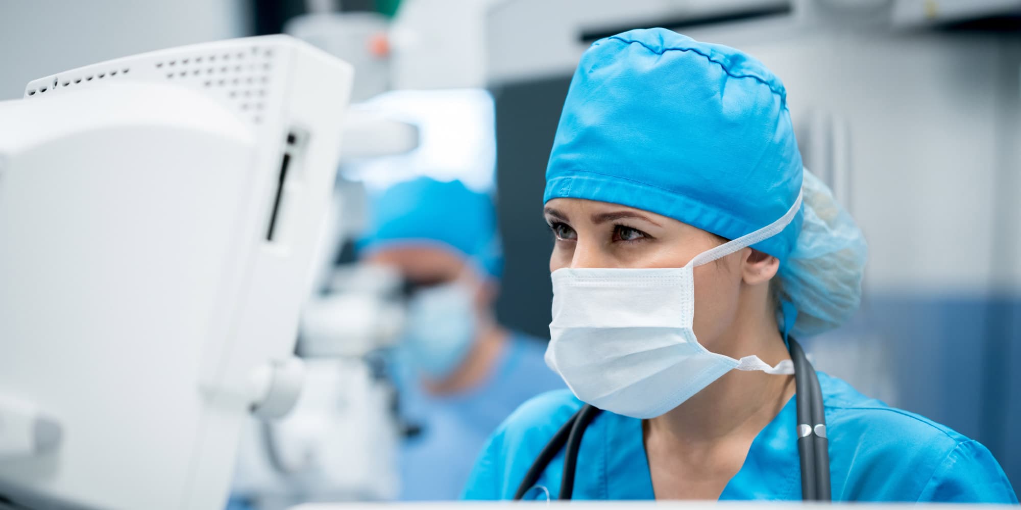 Medical-%26-pharma_0 Masked medical professional in blue scrubs working at a monitor in a hospital setting