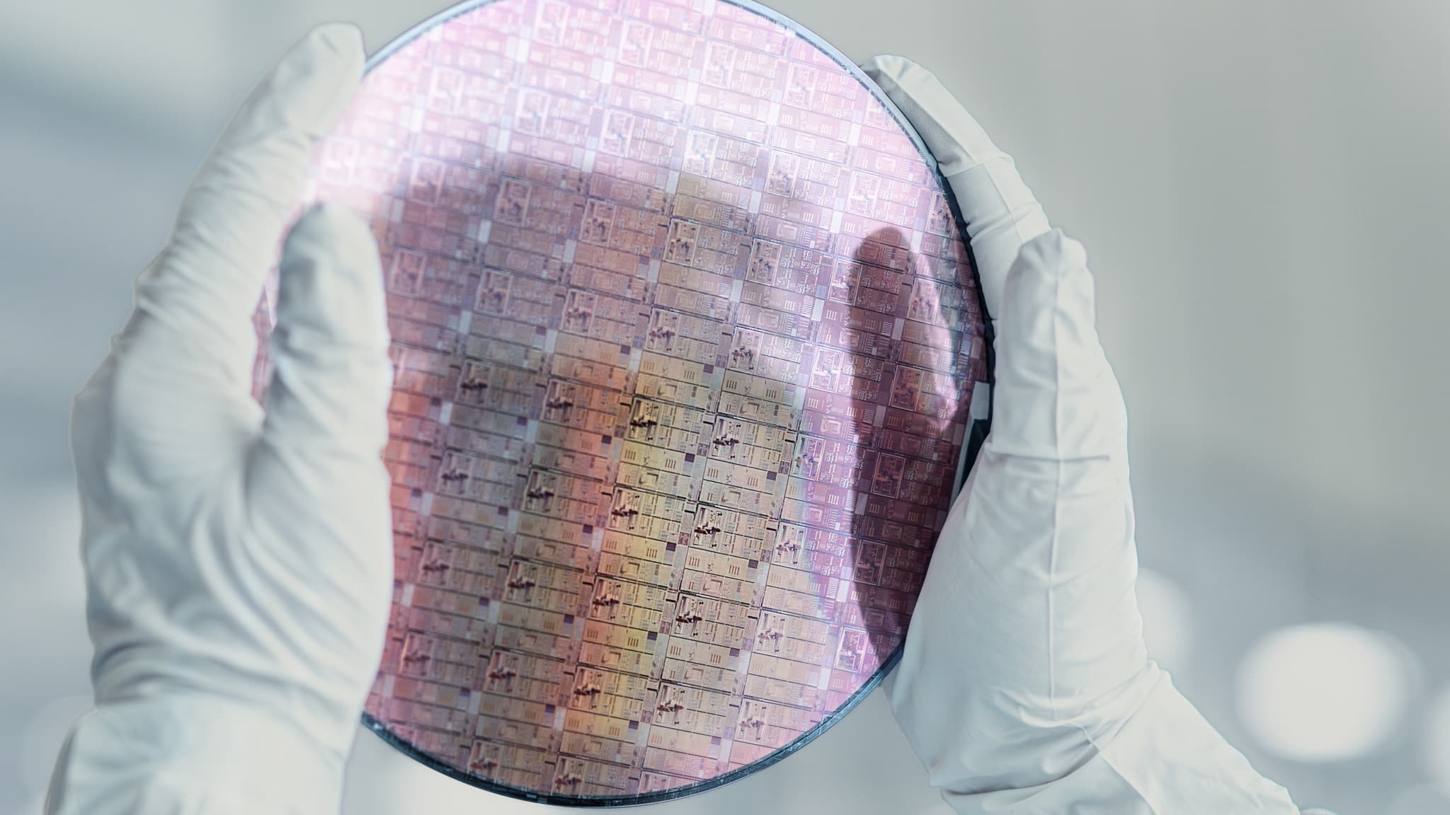 Semiconductor%20chip%20manufacturing Gloved hands holding a semiconductor wafer with patterned chip dies