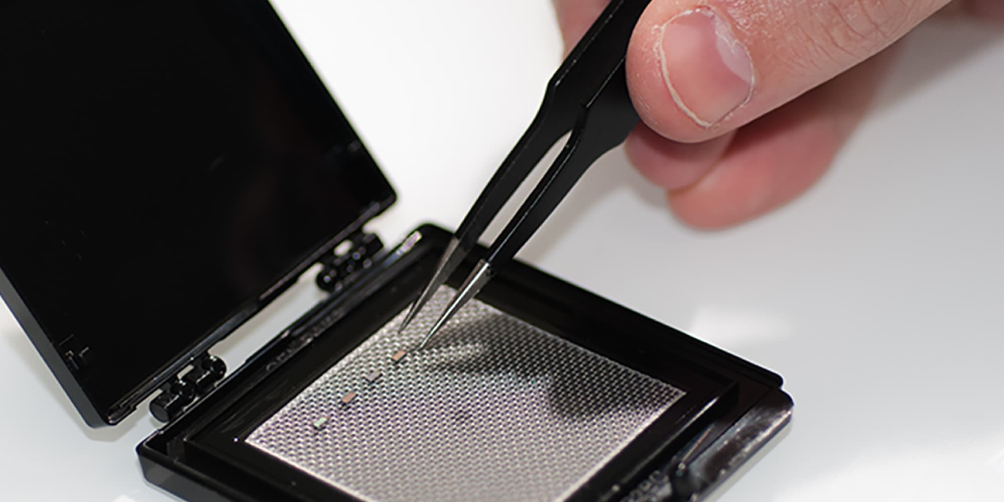 website_headers_2000x1000px Hand using tweezers to place a tiny chip in a black component case