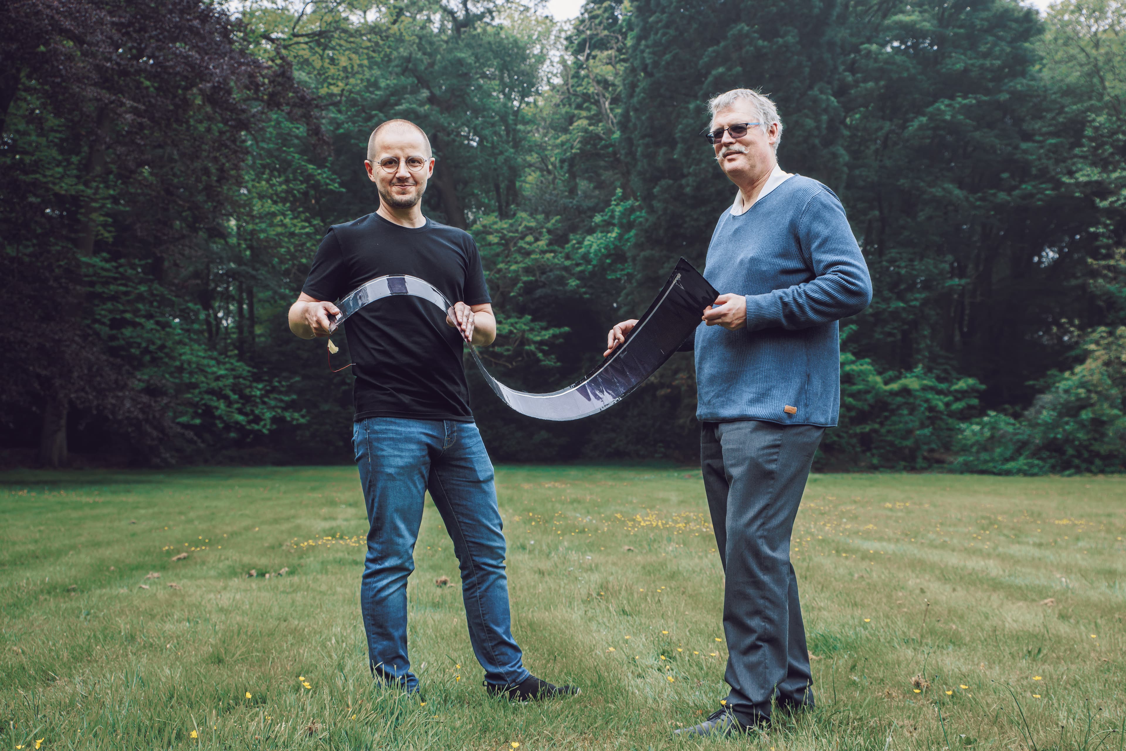 033_Bart%20Vermang_Marc%20Meuris_BLI_0221 Two men stand outdoors holding a flexible solar panel strip between them.