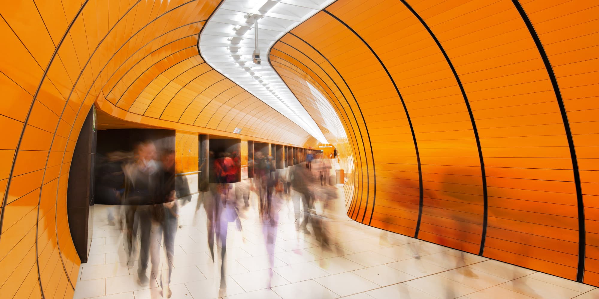 04-Liborg_1 Orange curved tunnel hallway with blurred people walking through it