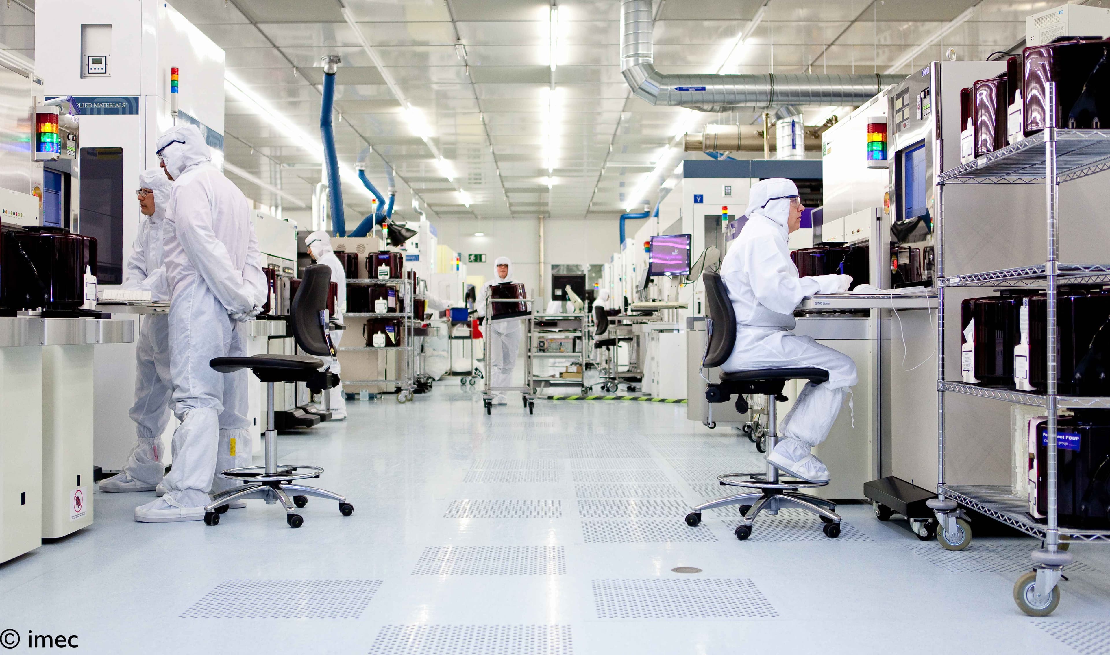 083-A-look-inside-imec%27s-300mm-cleanroom-2022_maxWidth_6144_maxHeight_3455_ppi_72_quality_100_embedMetadata_true_contentETag_7 Researchers in cleanroom suits working among semiconductor fabrication equipment in a spotless lab