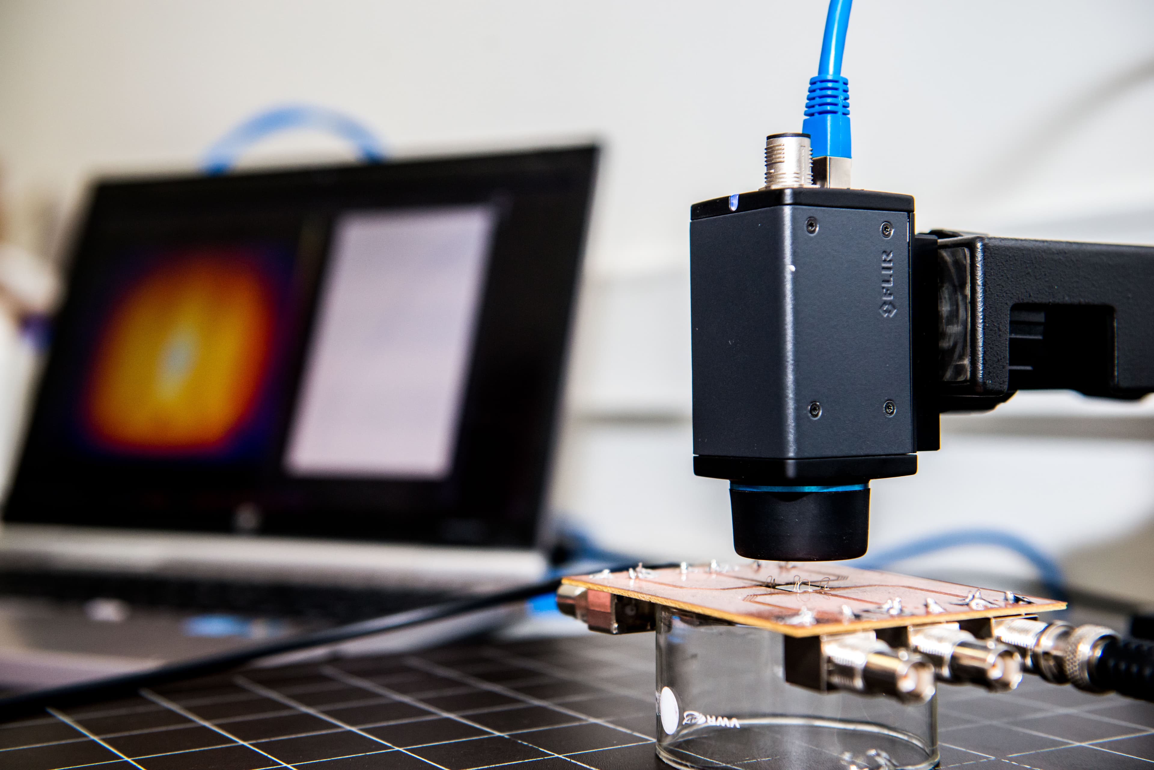 Microscope camera focusing on electronic sample in lab Microscope camera focused on a small electronic sample in a materials research lab, with a monitor in the background
