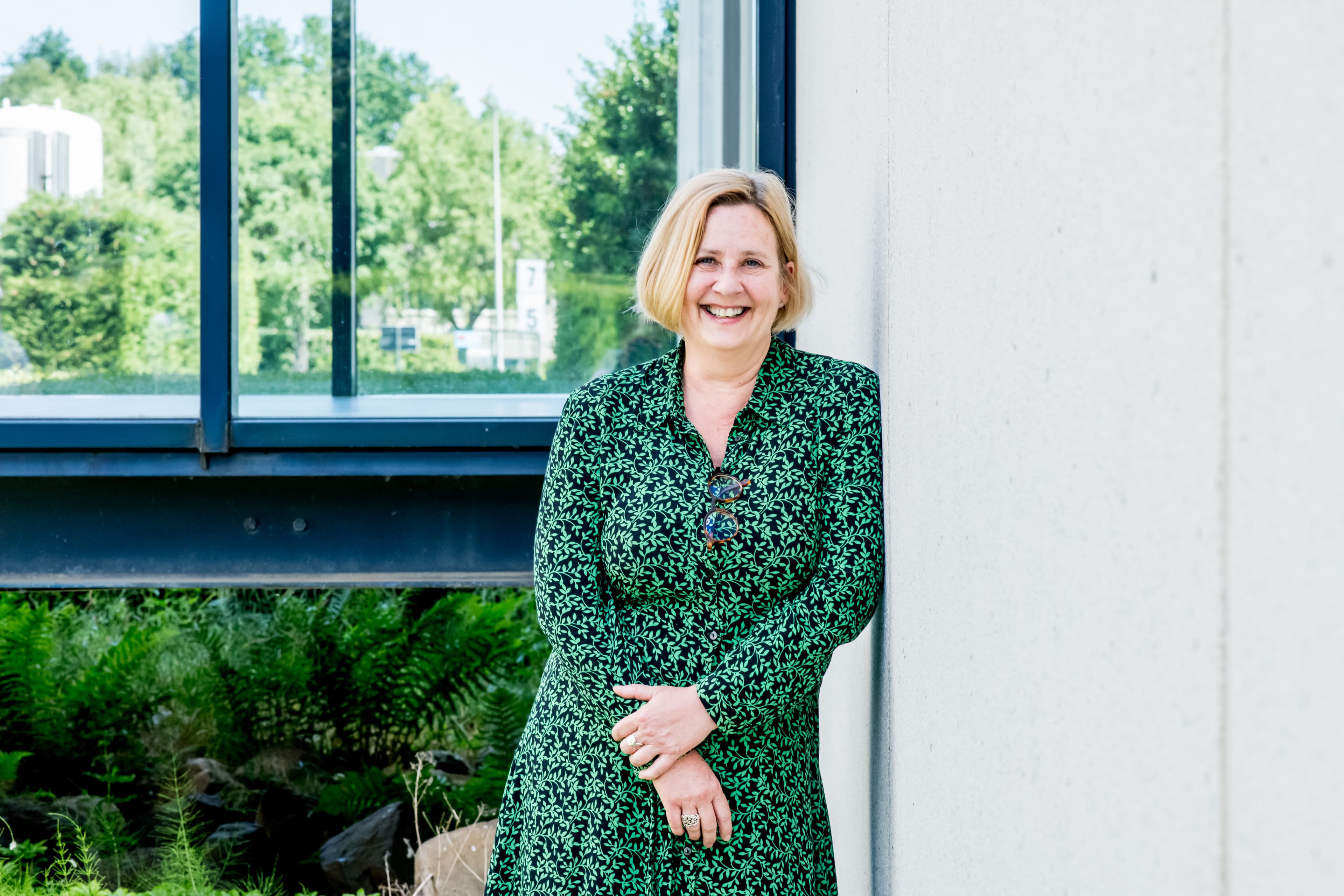1_Lieve%20DE%20DONCKER Lieve De Doncker smiling in a green patterned dress beside a windowed wall outdoors