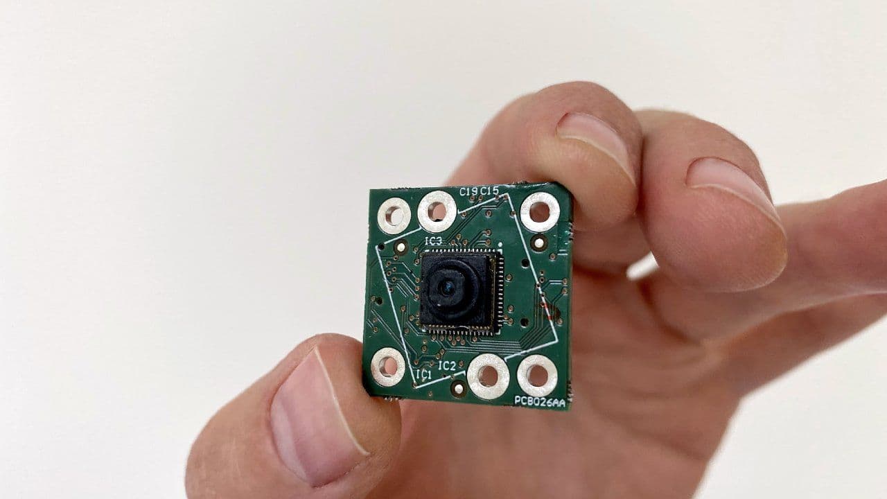 Hand holding small camera sensor circuit board Hand holding a small green sensor circuit board with a tiny camera lens chip in the center
