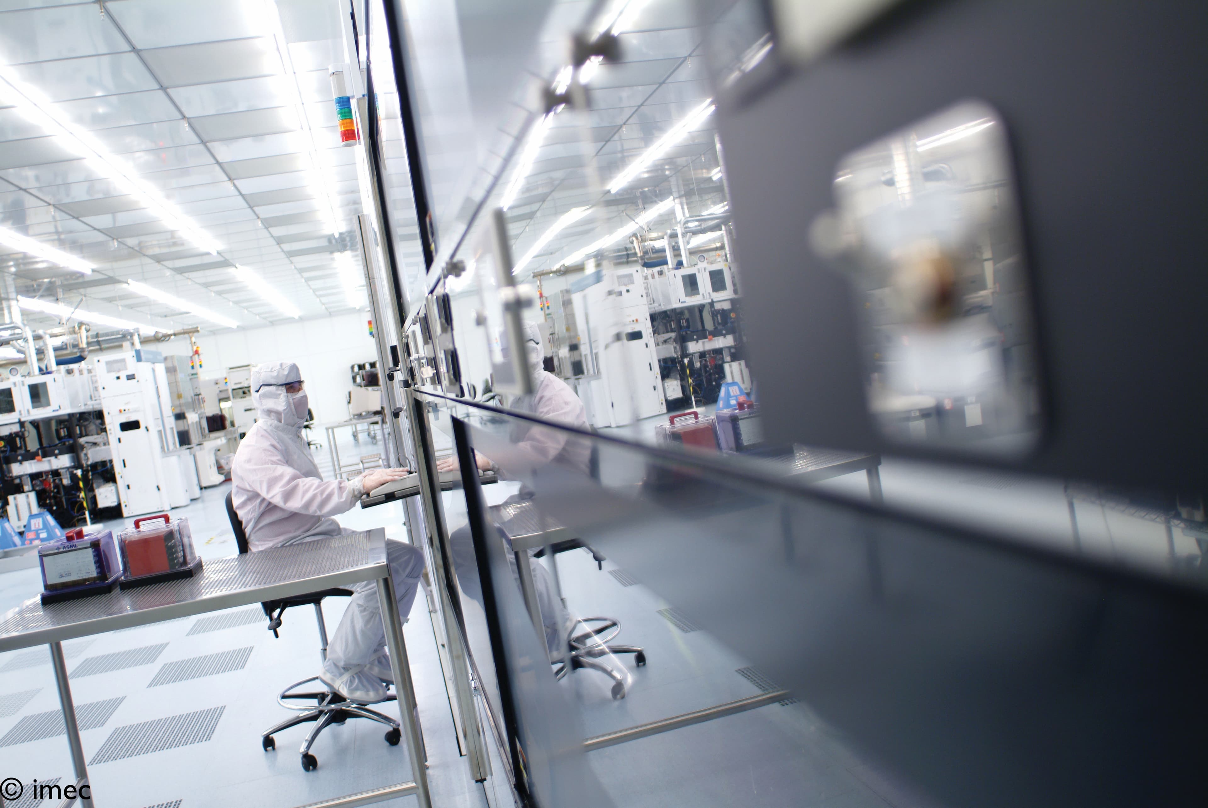 188-A-look-inside-imec%27s-300mm-cleanroom-2022 Technician in a cleanroom working beside semiconductor equipment through a glass partition