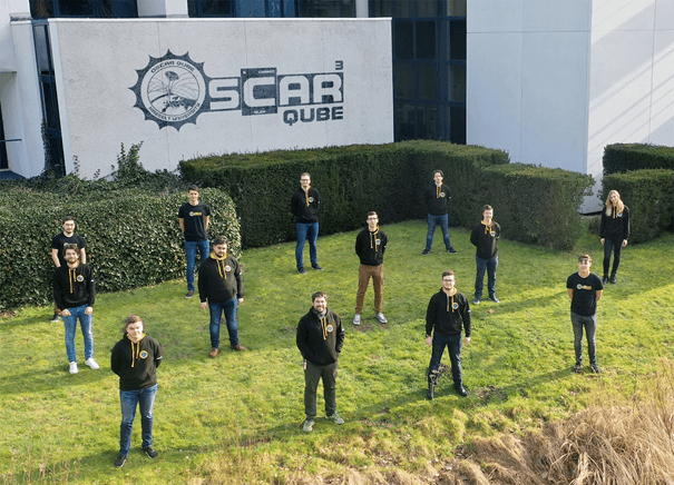 2_OscarQubeTeam OSCAR-QUBE team standing on grass in front of the imo-imomec building and project logo