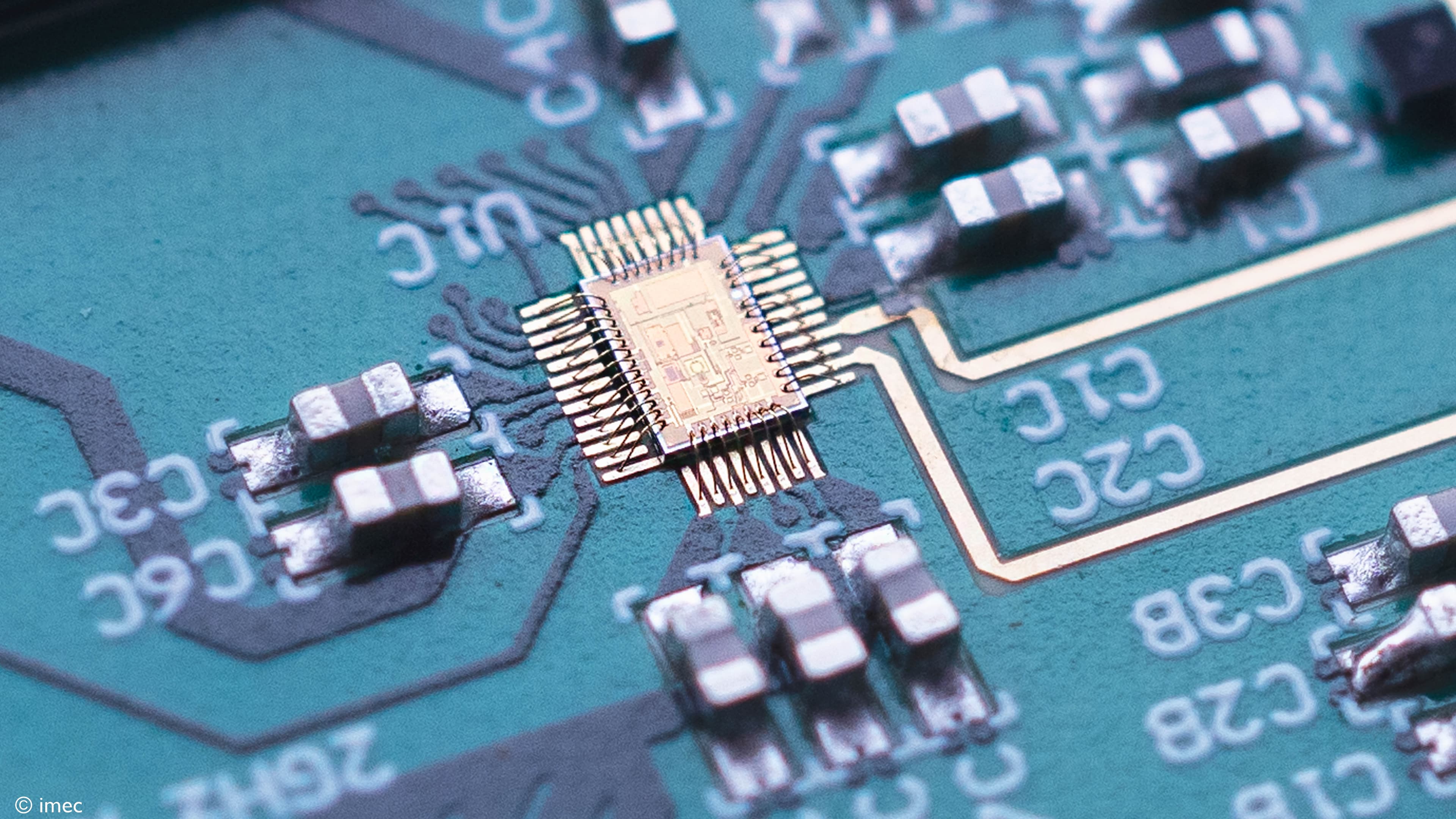 214-Novel-charge-pump-PLL-integrated-with-imec%E2%80%99s-existing-140GHzradar-receiver-and-transmitter002 Close-up of a microchip on a circuit board with surrounding surface-mount components.
