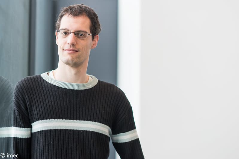 2587920717519a0010ef_c_1 Portrait of Nick Van Helleputte, wearing glasses and a dark striped sweater, standing indoors by a window