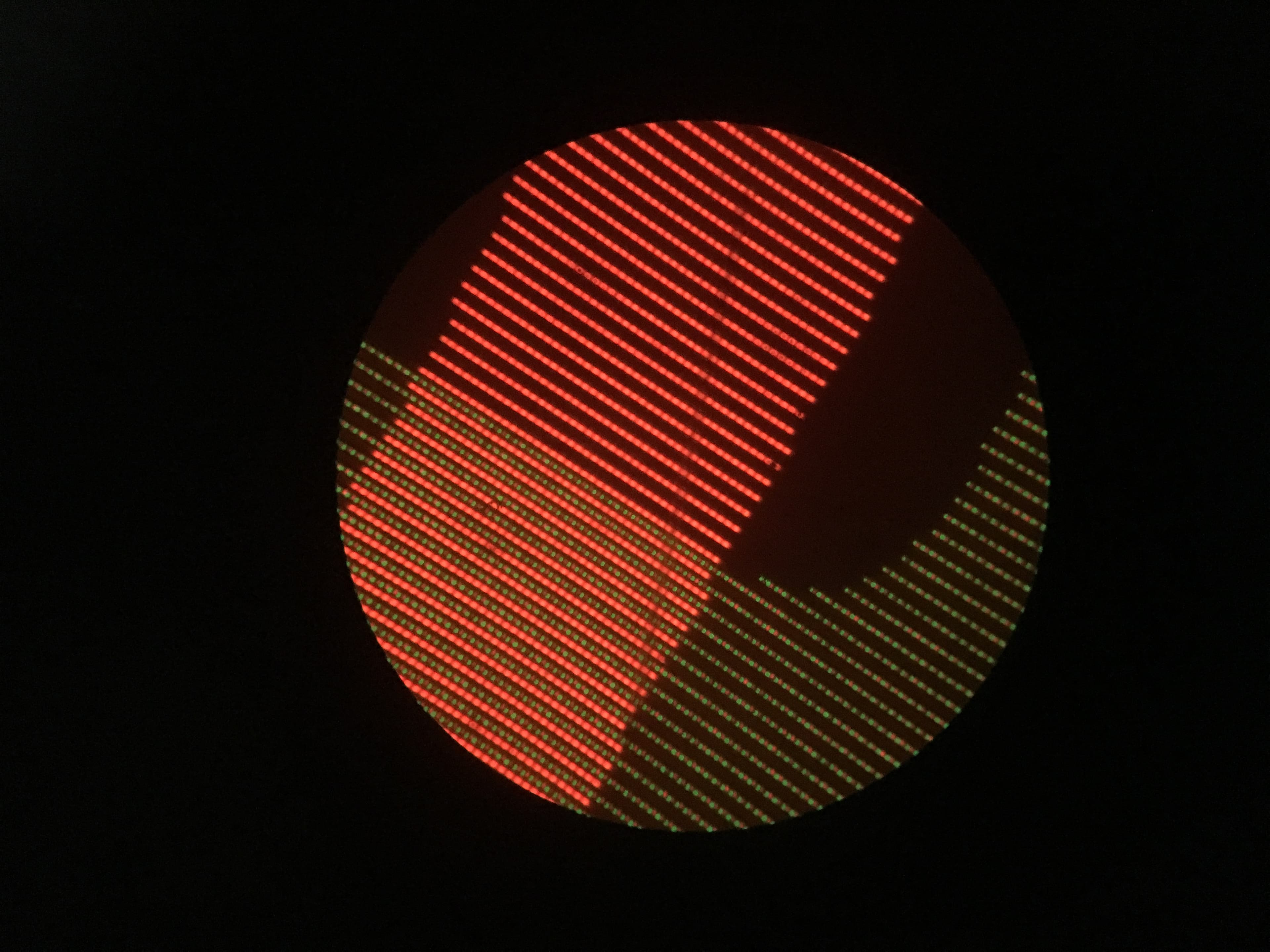 2ColorDisplay Close-up van een cirkelvormig OLED-scherm met rode en groene pixelrijen op een zwarte achtergrond.