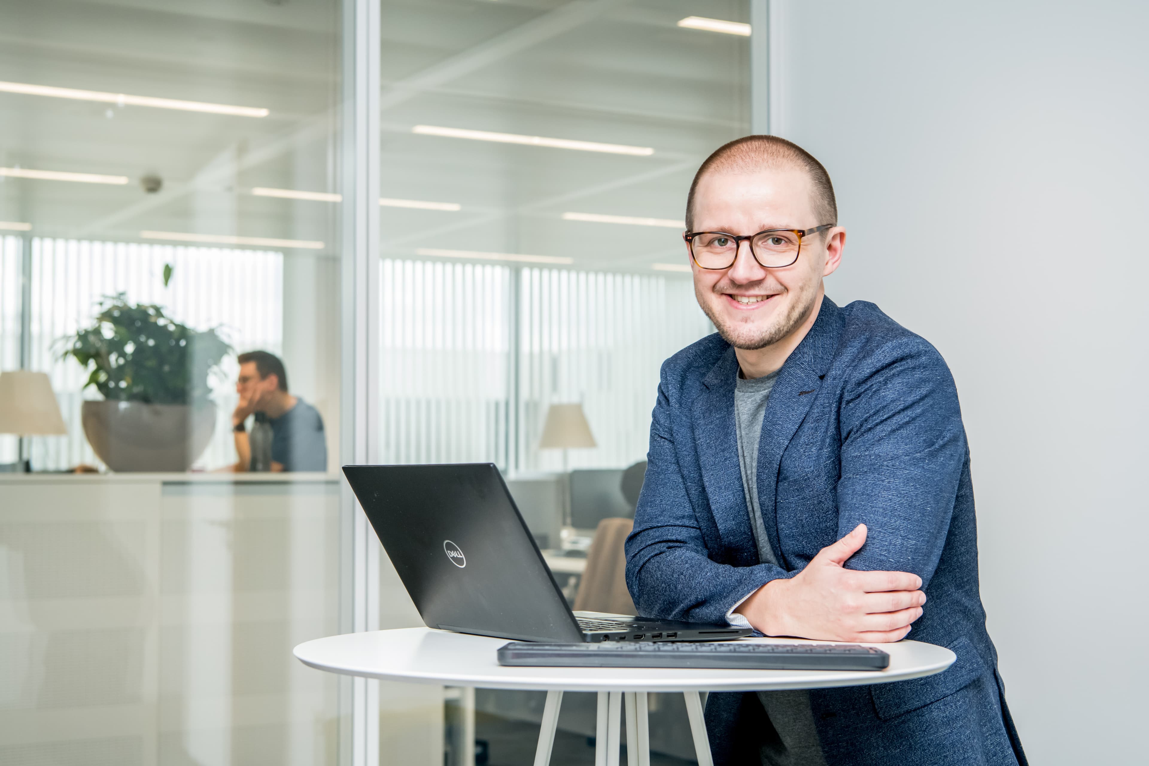 4_bart_vermang Bart Vermang seated at a table with a laptop in a modern office, smiling at the camera.