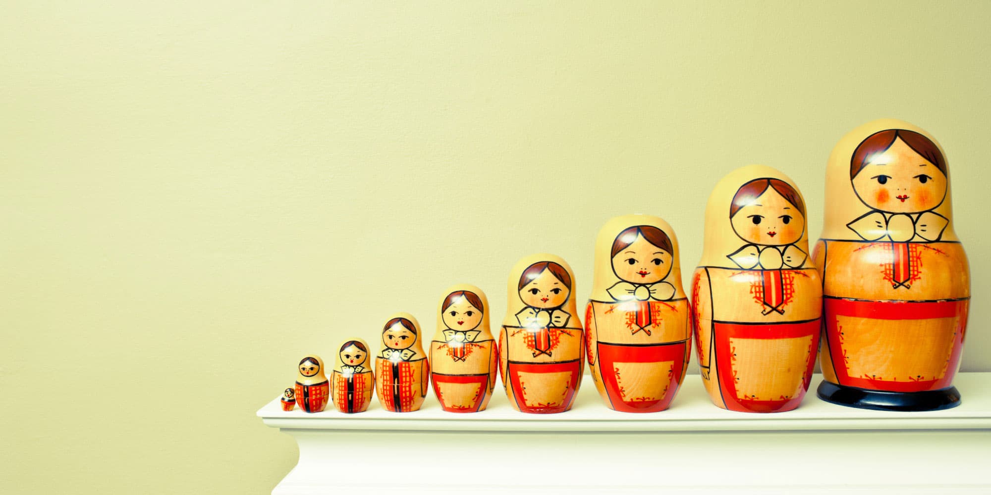 5_Museic-chip_spiegel_1 Row of nested wooden matryoshka dolls on a white shelf against a pale wall