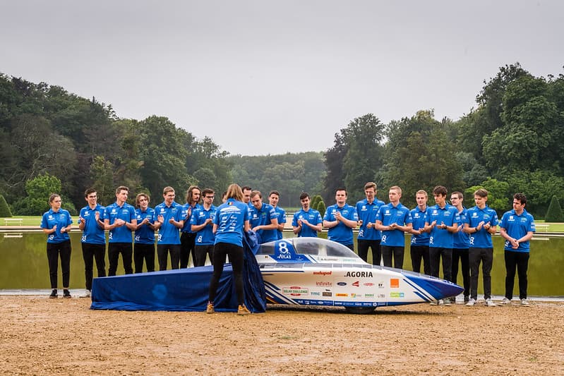 51354291534_54a4f0803f_c Het Agoria Solar Team onthult een blauw-witte zonne-raceauto, met het team erachter bij een vijver.