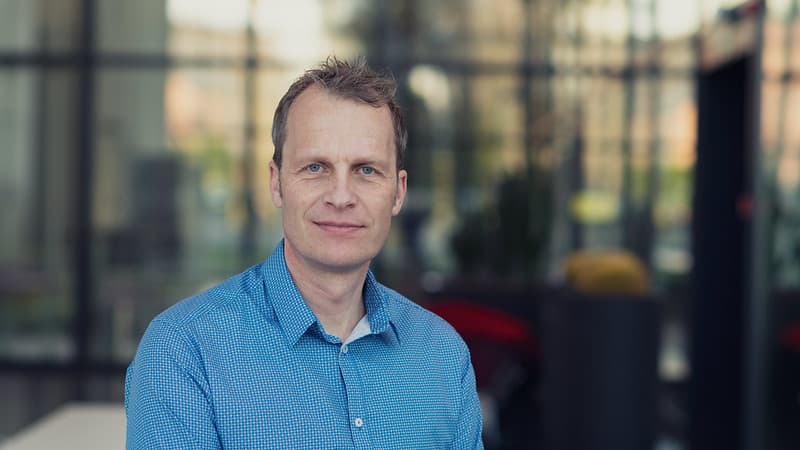 portrait of a man in a blue shirt indoors Lars-Åke Ragnarsson in a blue shirt, standing indoors against a blurred glass background.