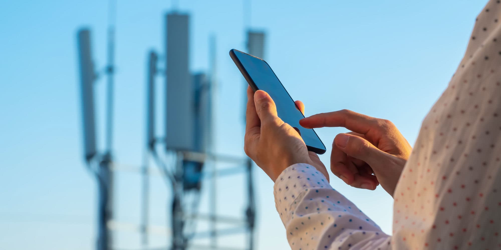 5G-straling-onderzoek-header Person using a smartphone near 5G antennas against a blue sky