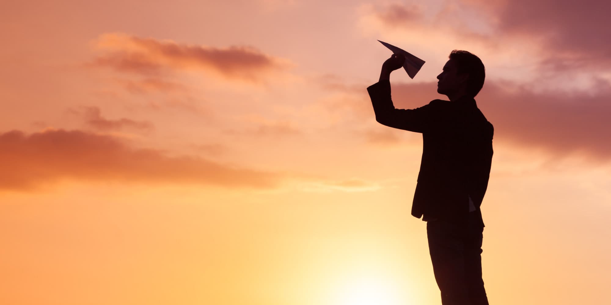 6.-venturing_1 Silhouetted person launching a paper airplane against a sunset sky