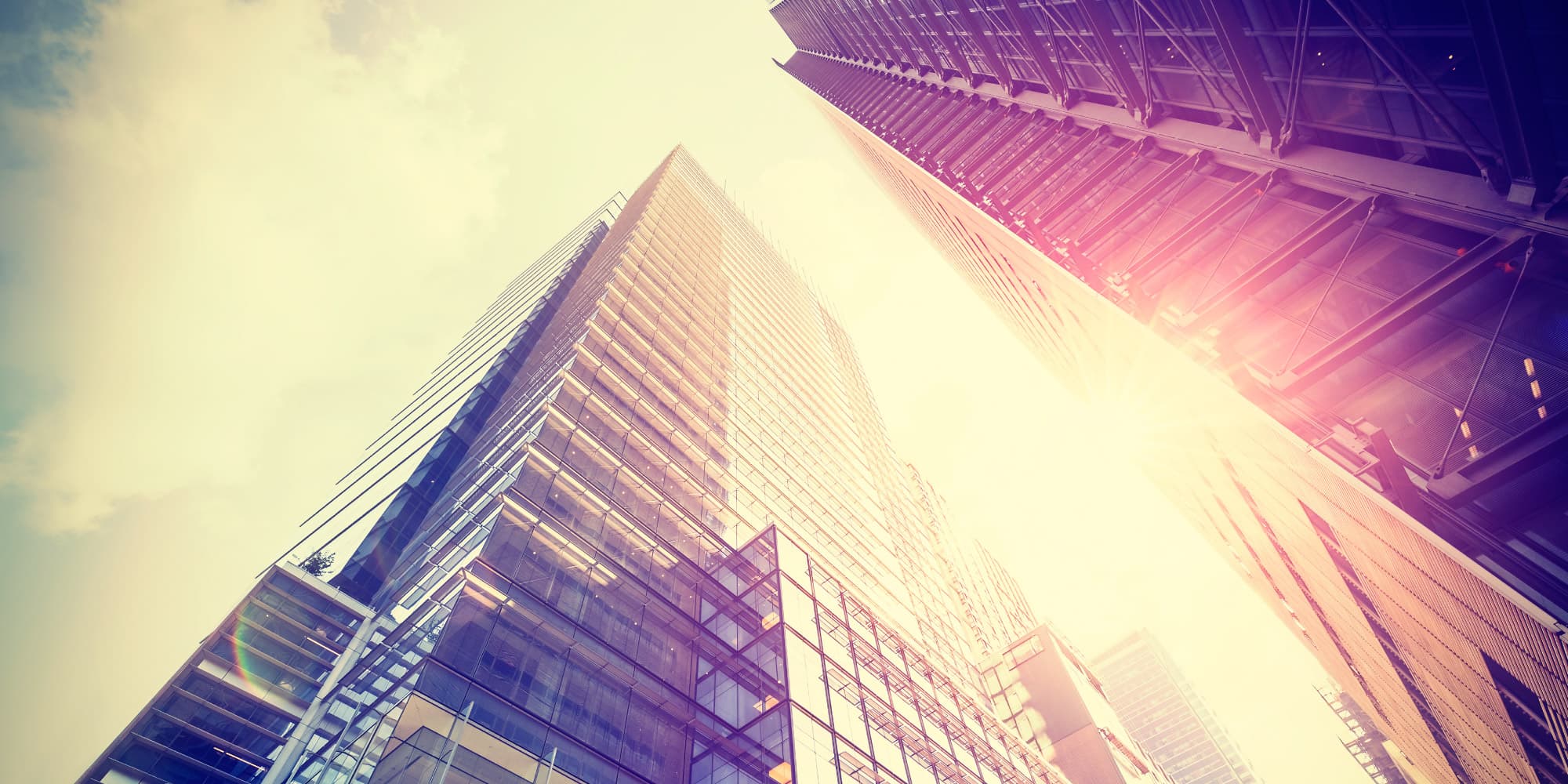 7.-zonnegevels-als-energiebron_1 Sunlit modern office towers with reflective glass facades viewed from below