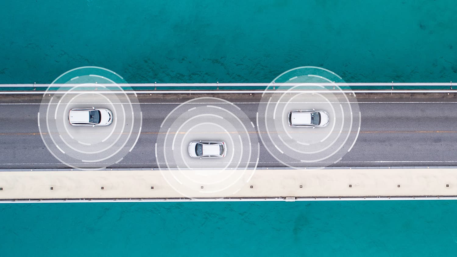 aerial_resize Drie auto’s op een brug boven turquoise water, met cirkelvormige sensorgrafieken die autonoom rijden suggereren