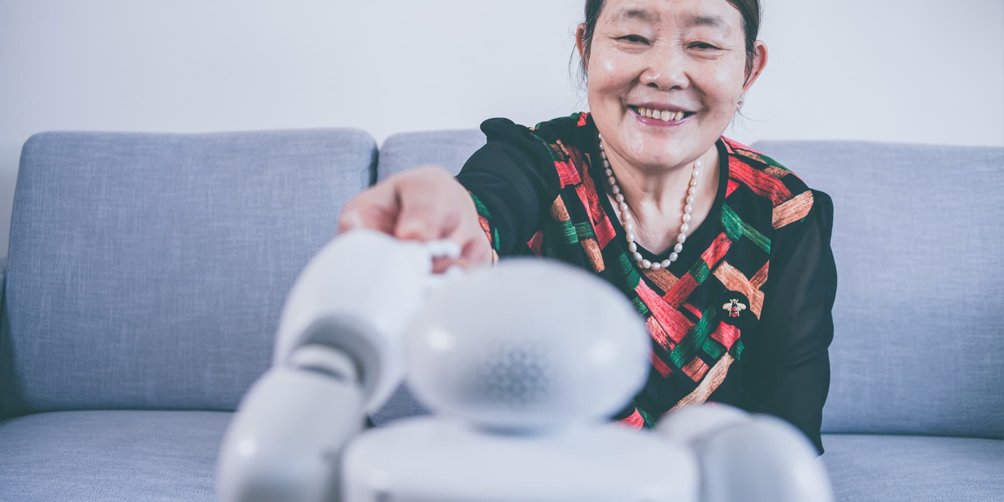 AI_carerobot Glimlachende vrouw die reikt naar een kleine robot op een sofa