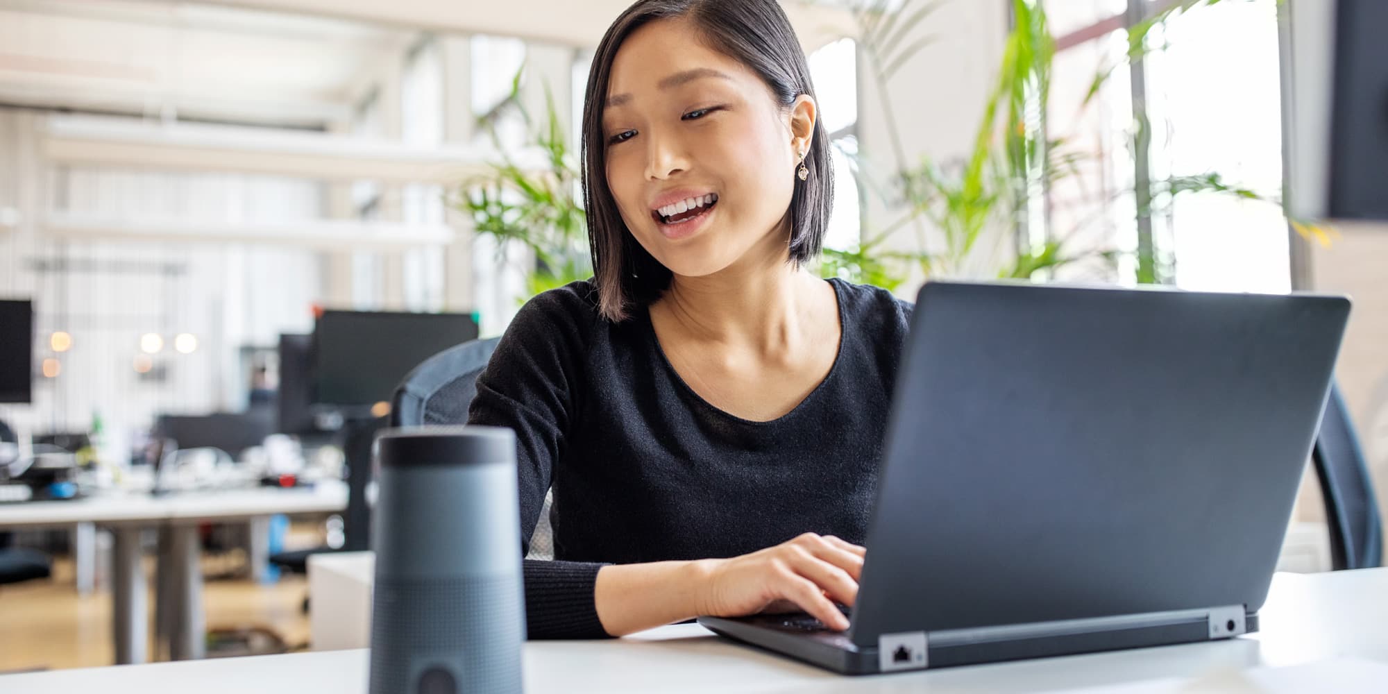 AI_smartspeaker Vrouw die een laptop gebruikt naast een slimme speaker in een kantoor
