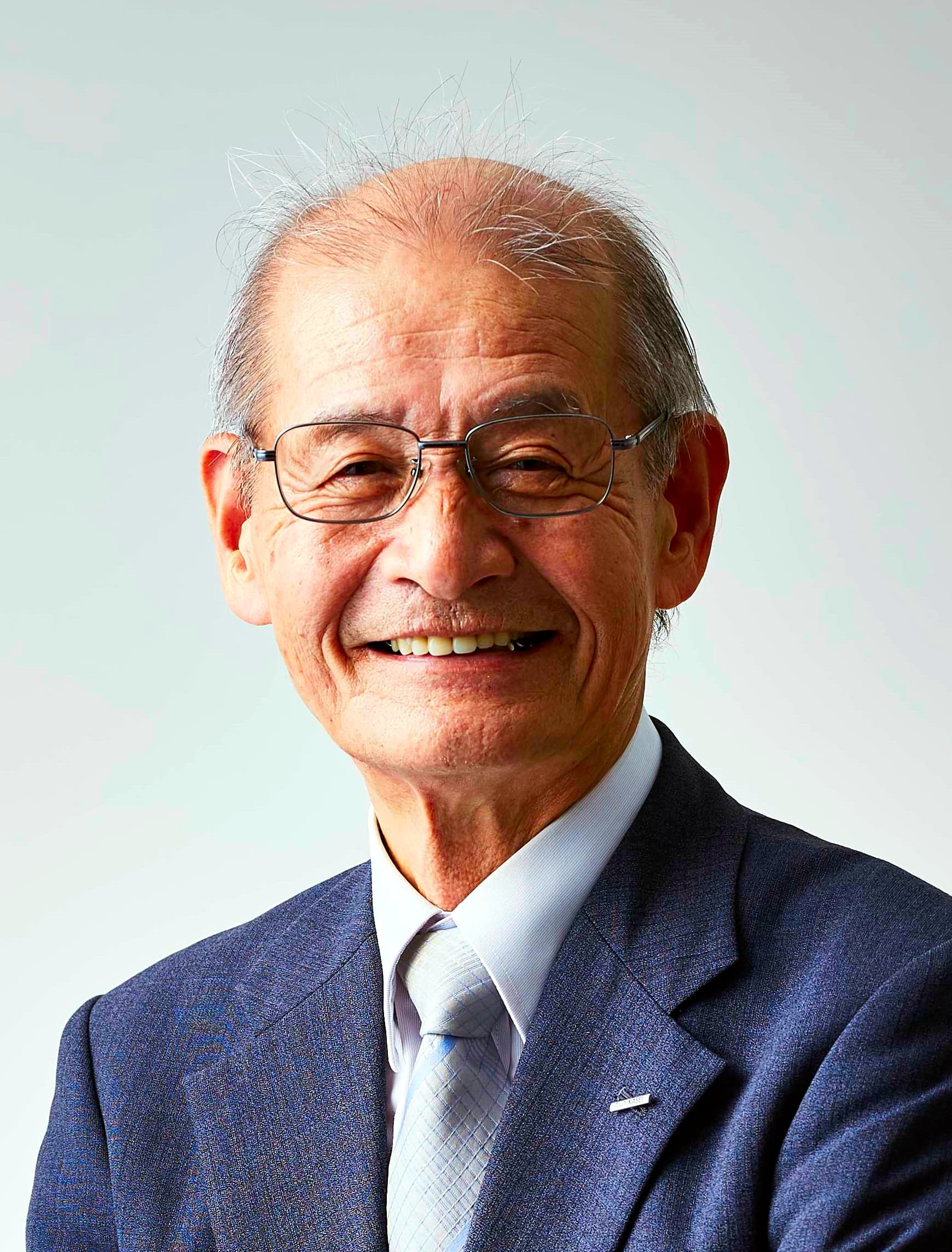 Akira_Yoshino_cropped_2_Akira_Yoshino_201911 Portret van Akira Yoshino in een pak en bril, glimlachend tegen een effen lichte achtergrond.