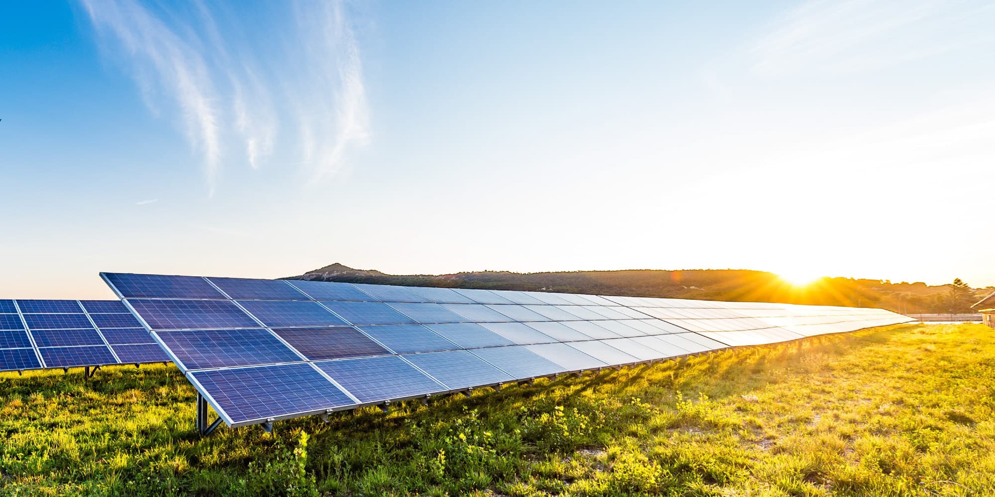 analyst-pv_1 Zonnepanelen in een veld bij zonsondergang met een felle zonneschittering boven de horizon