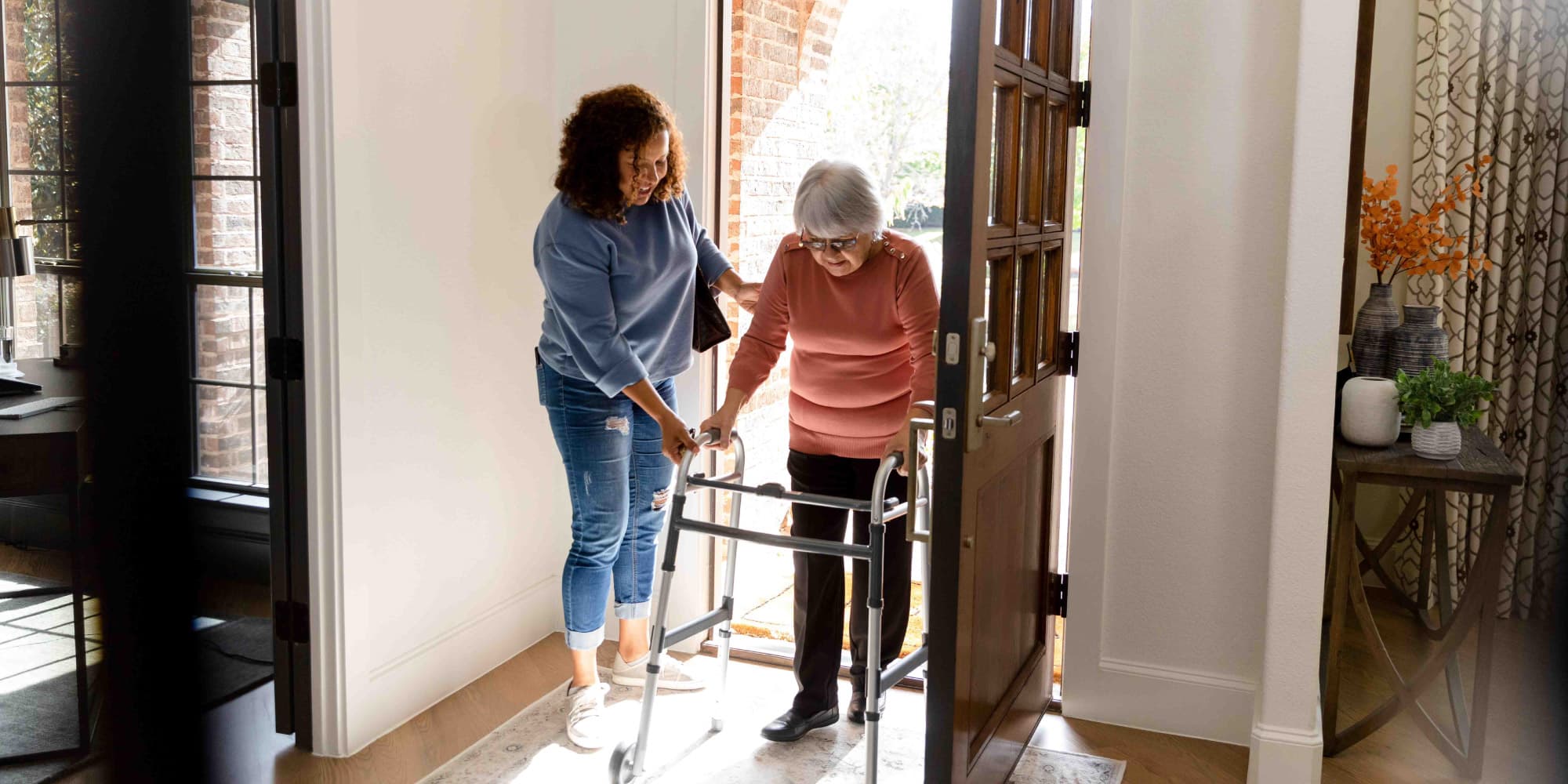 article-protego Verzorger helpt een oudere vrouw met een rollator bij de voordeur van een huis