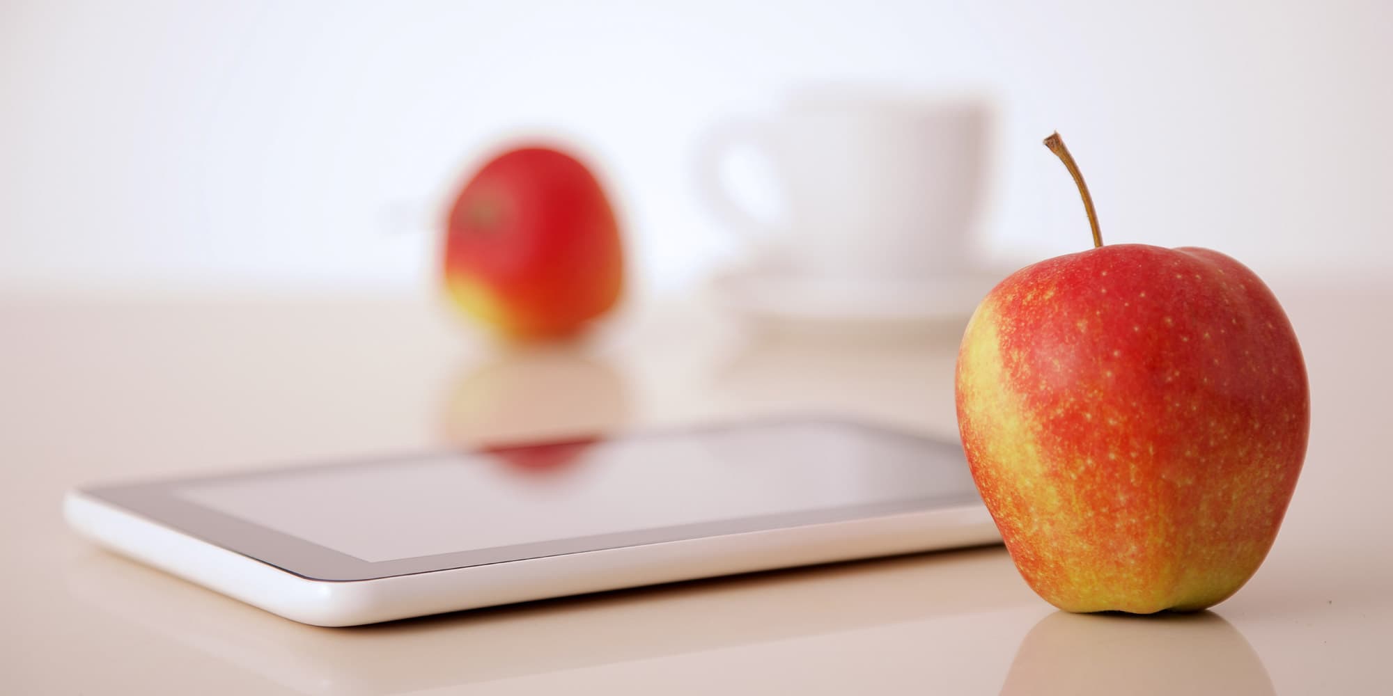 Articles-Gezondheidszorg-zullen Appel naast een tablet, met een wazige appel en kopje op de achtergrond