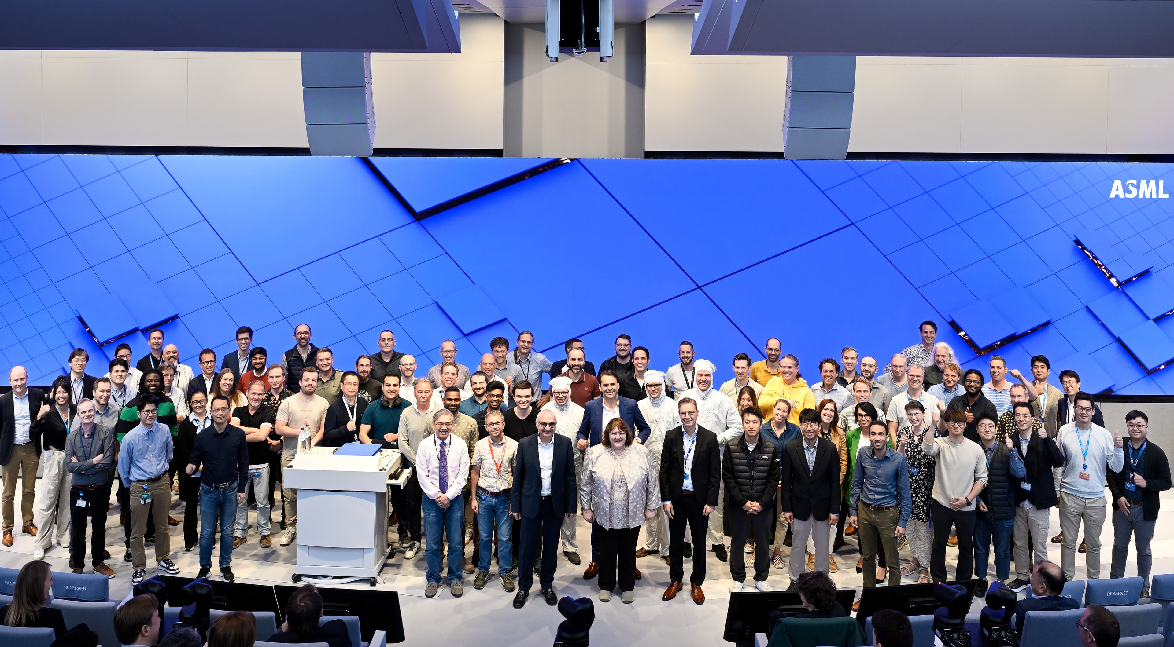 ASML%20High%20NA%20Lab%20Opening%20Celebration%203-2 Large group posing on stage in front of a blue ASML backdrop at the High NA lab opening celebration