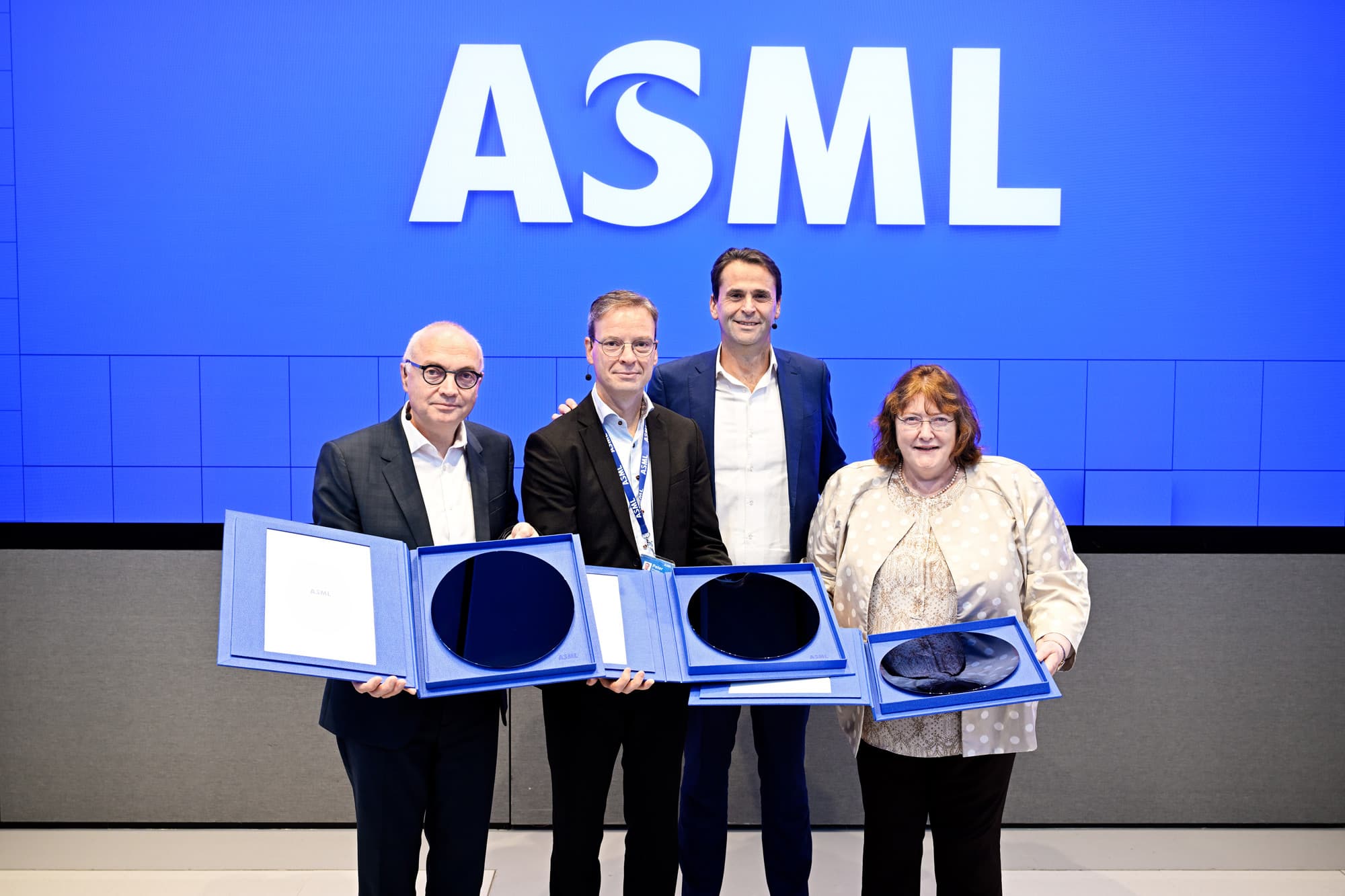 ASML-High-NA-Lab-Opening-Celebration-resized Vier leidinggevenden die presentatiedozen vasthouden met zichtbare wafers voor een groot ASML-bord.