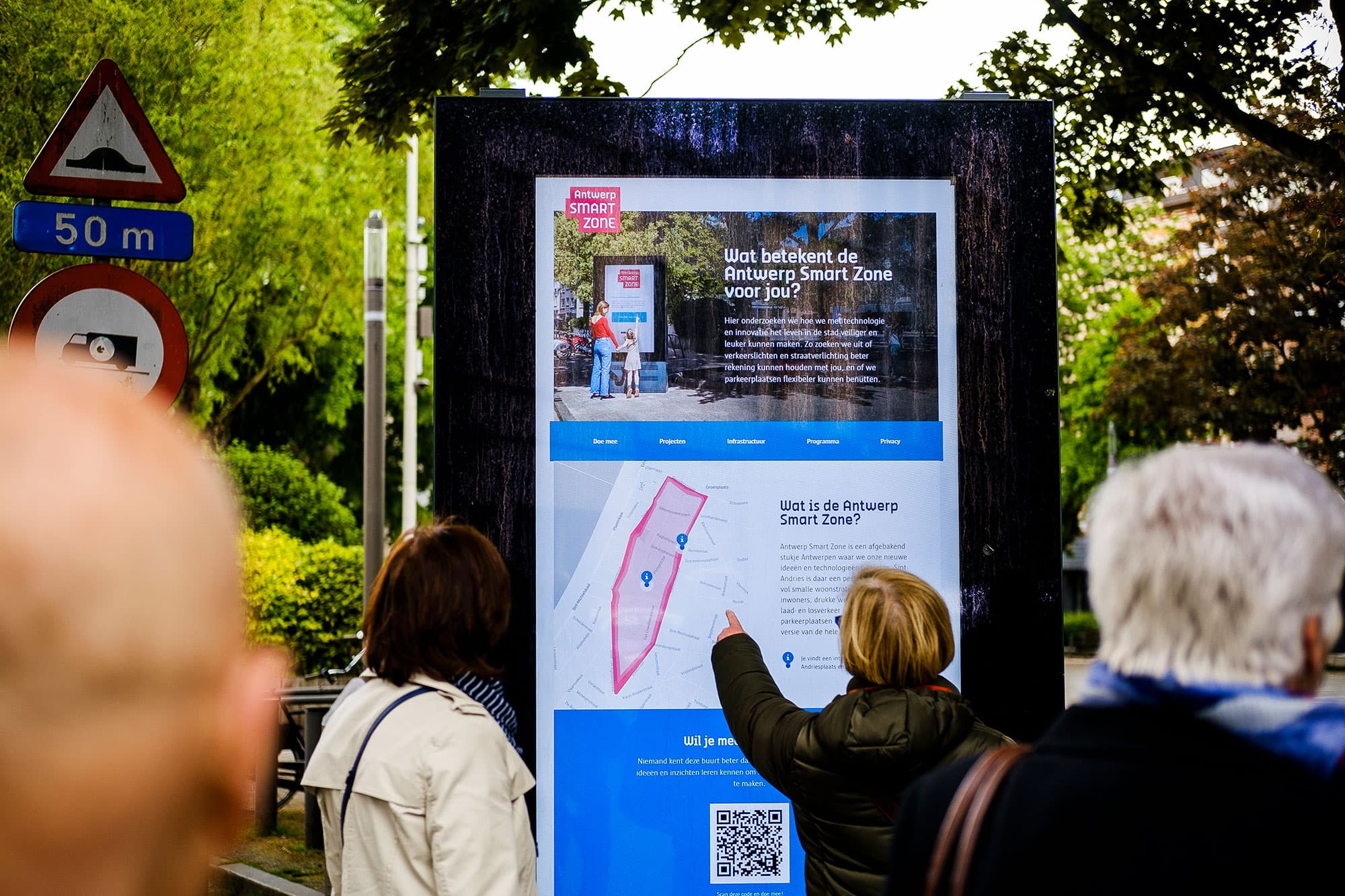 ASZ_0 Mensen die buiten naast een verkeersbord een informatiebord van de Antwerp Smart Zone bekijken