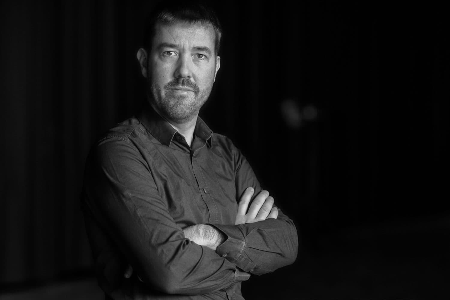 Bart_Onsia_1 Portret van Bart Onsia, met gekruiste armen tegen een donkere achtergrond