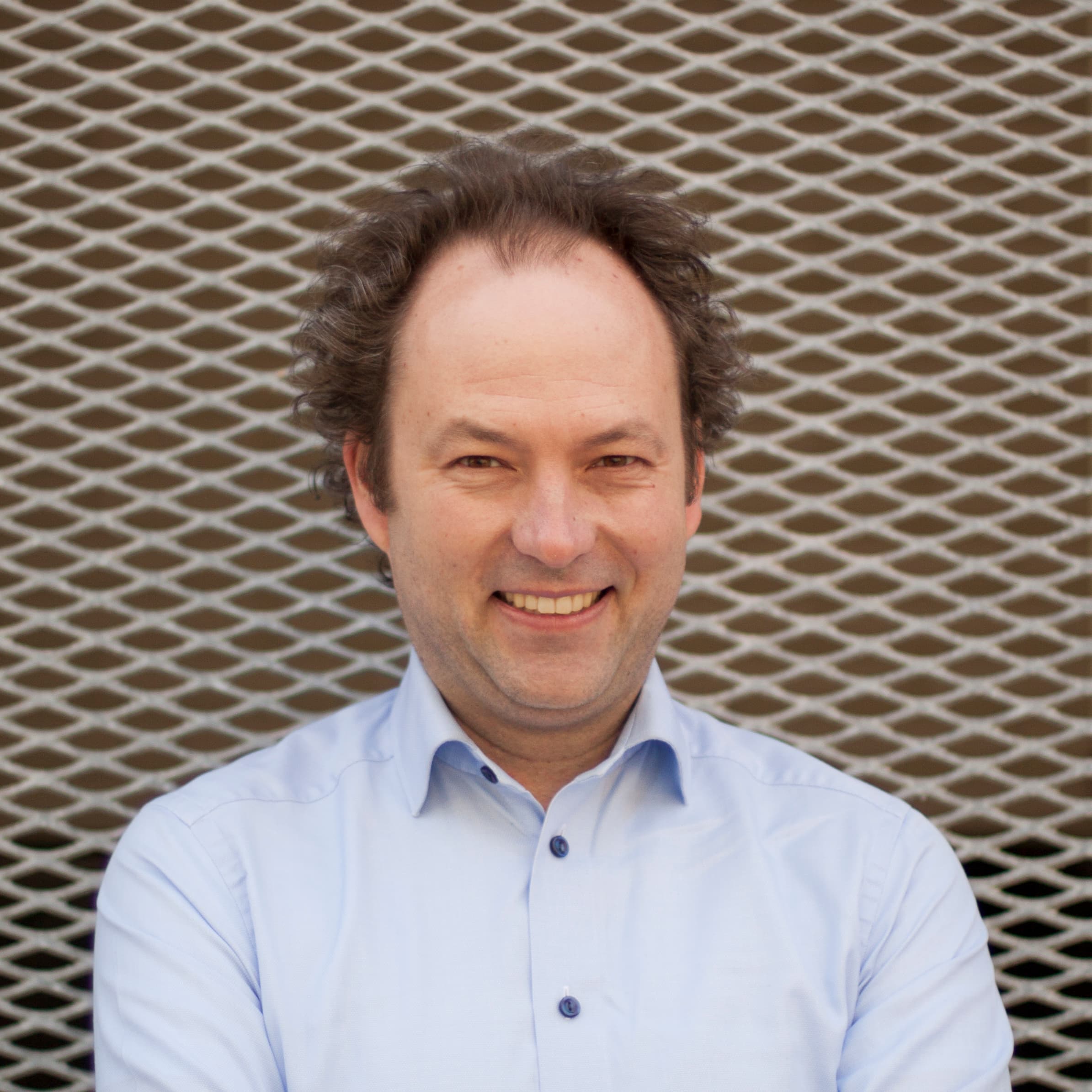 BartLannoo_Foto_March2018_1 Head-and-shoulders portrait of Bart Lannoo in a light blue shirt against a metal mesh background.