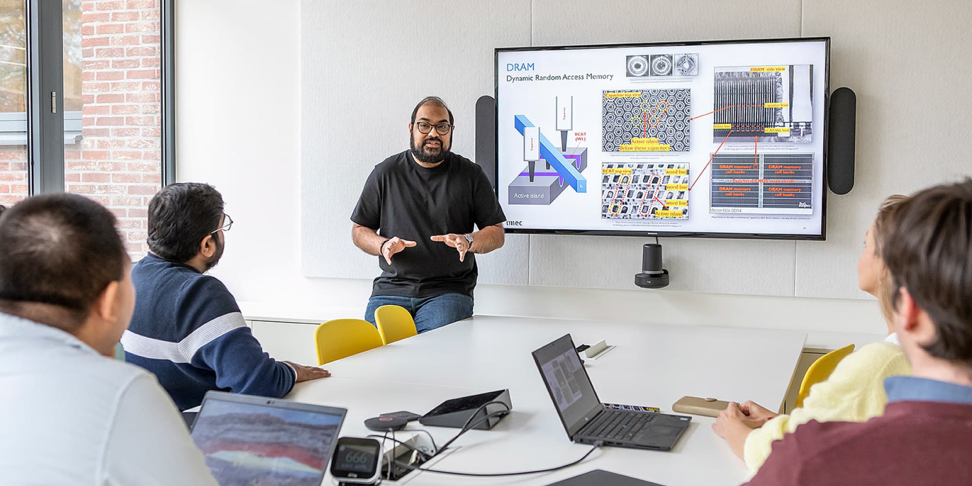 Bilateral-research Researchers in a meeting room watch a presenter explain DRAM memory diagrams on a large screen.