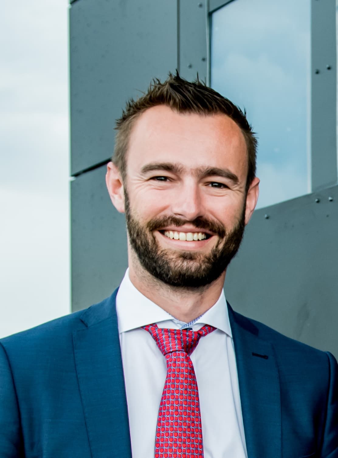 biofoto_michael_1 Smiling man in a blue suit and red tie, posed for an author portrait