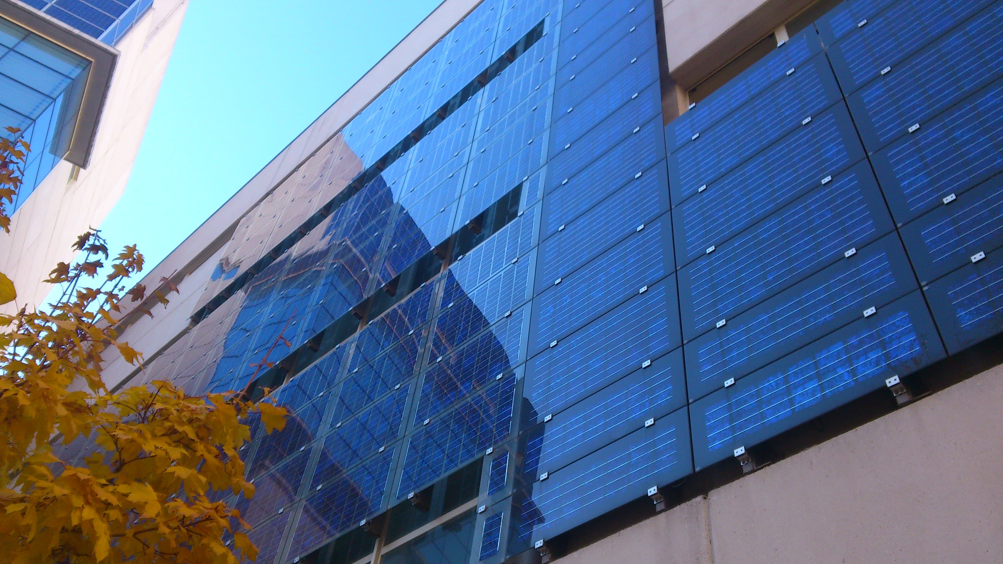 BIPV_solar-facade Modern building facade covered with blue solar panels, seen from below against a clear sky