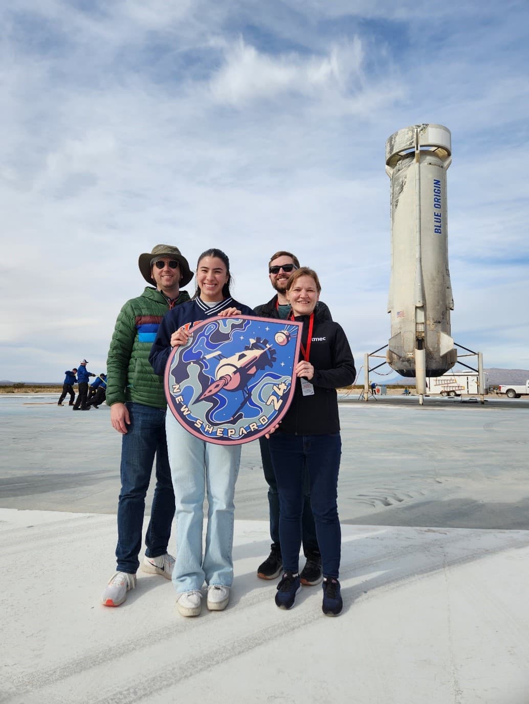 BlueOrigin_NS_Team Team members posing beside a Blue Origin New Shepard rocket on the launch pad.
