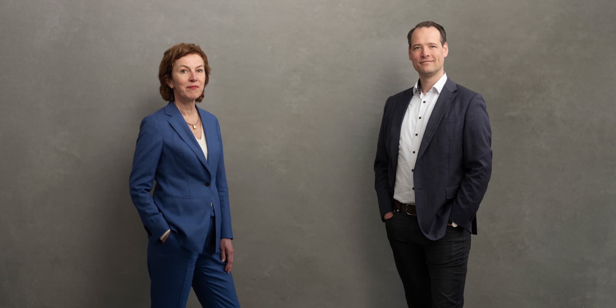 Can-technology-make-healthcare-more-human Two professionals in suits pose against a plain gray backdrop