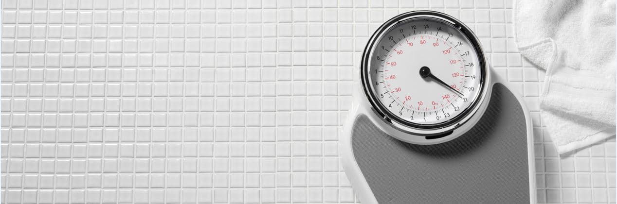 Bathroom scale with dial and towel on tiled floor Bathroom scale with a dial on a tiled floor and a folded towel nearby