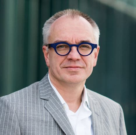 Capturechrisvanhoof_1 Portrait of Chris Van Hoof wearing blue glasses and a gray pinstripe jacket