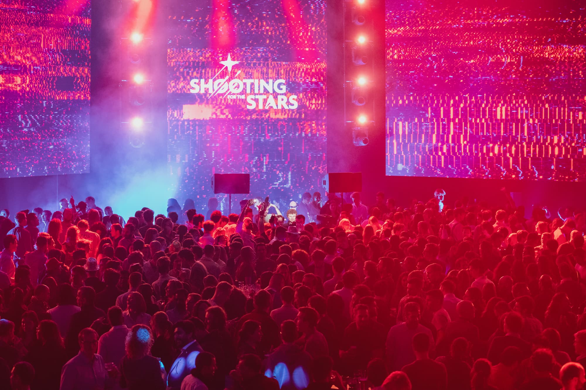 Crowd at 'Shooting for the Stars' event Crowd gathered at a brightly lit event stage with 'Shooting for the Stars' on the screens