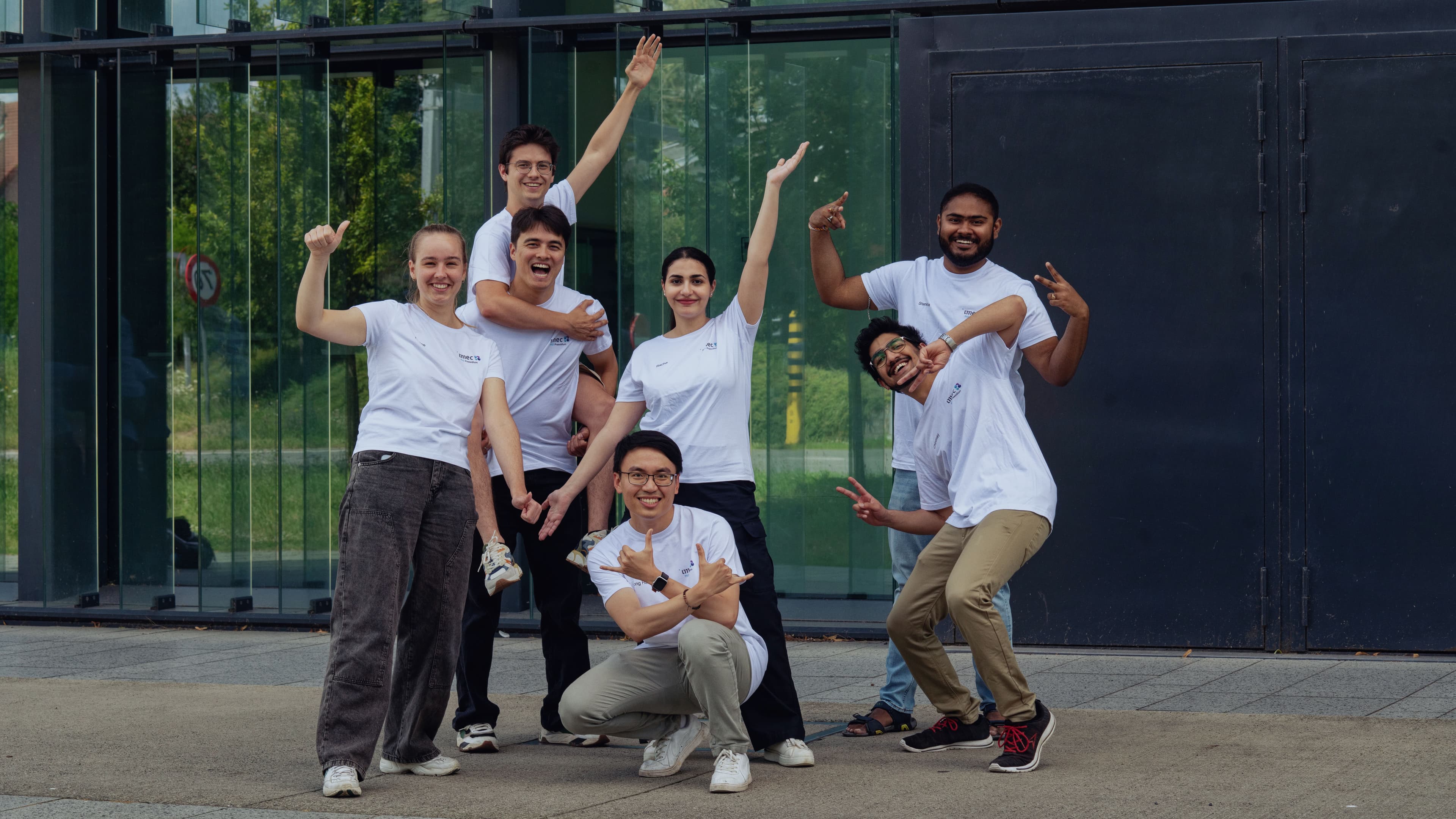 Carroussel%203 Group of imec employees posing and smiling outside a glass building in white T-shirts