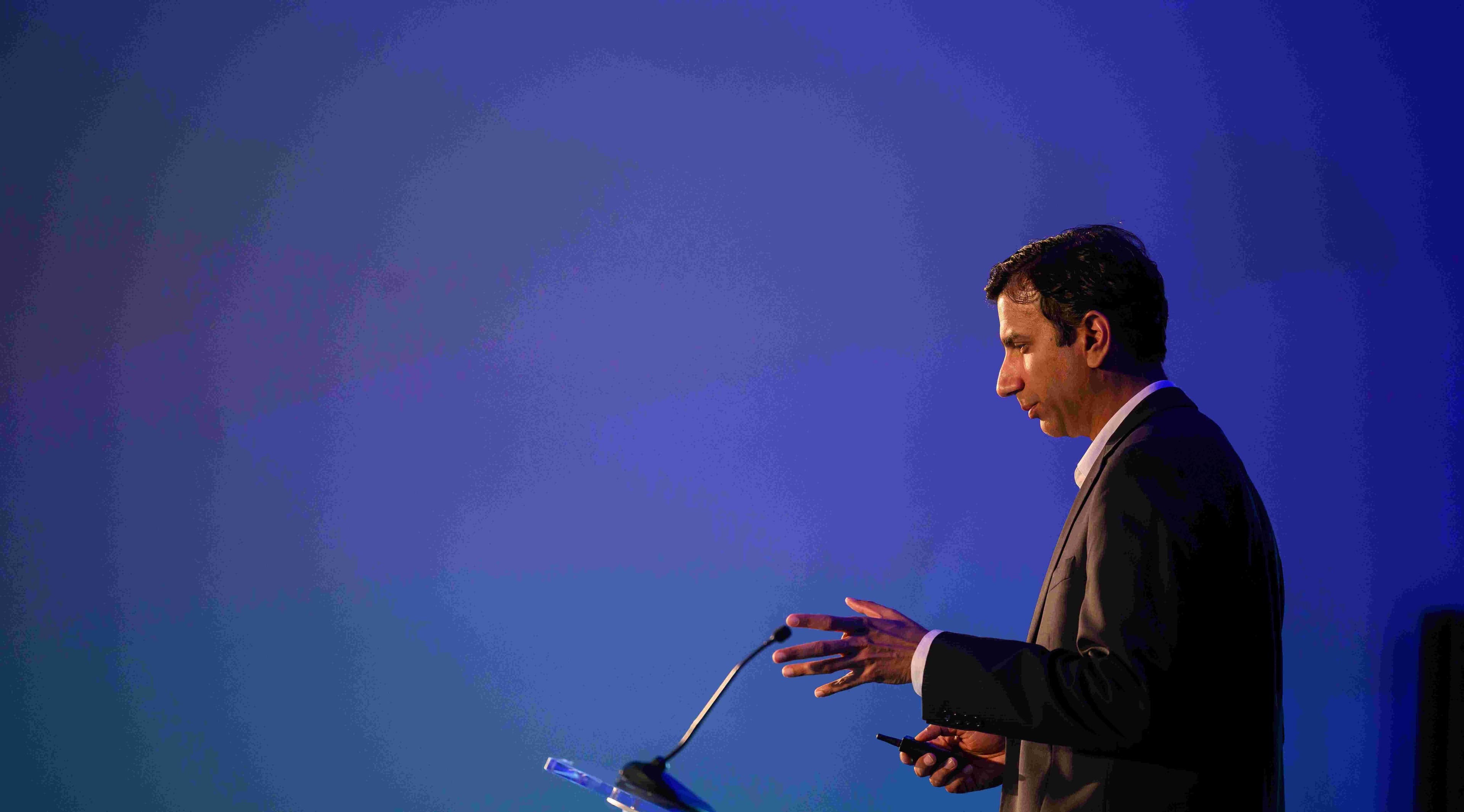 Celestial%20AI%20imec Man in a suit speaking at a podium on a blue-lit stage