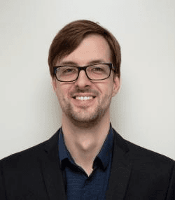christiaan%20bachmann Portrait of Christian Bachmann, smiling in glasses and a dark blazer against a light background
