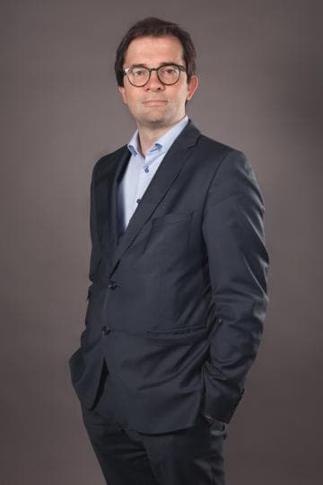 Claes_foto_1 Portrait of Stephan Claes in a dark suit and glasses against a neutral background.