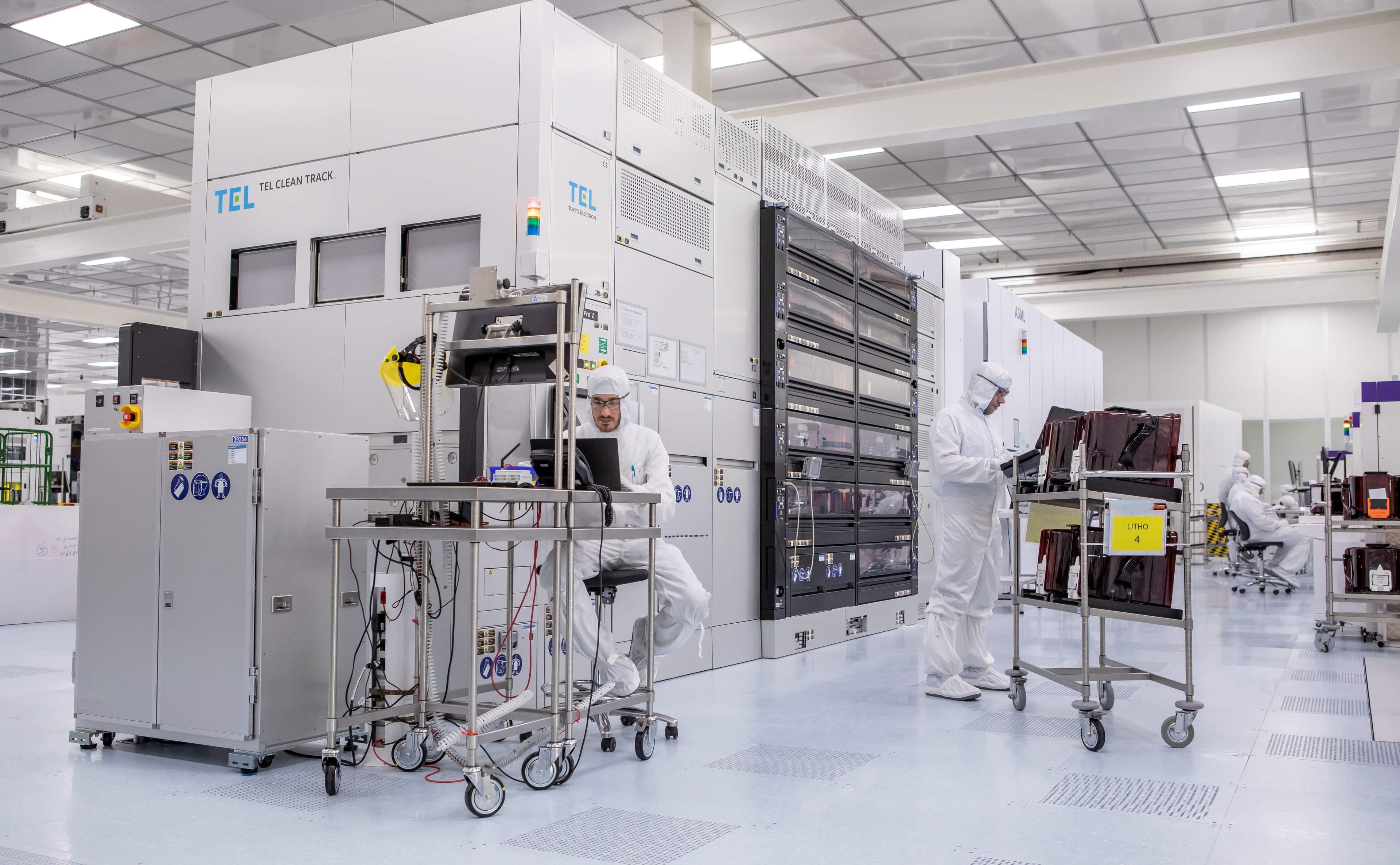 CLEANROOM30 Onderzoekers in cleanroomkleding werken naast halfgeleiderverwerkingsapparatuur in een cleanroom.